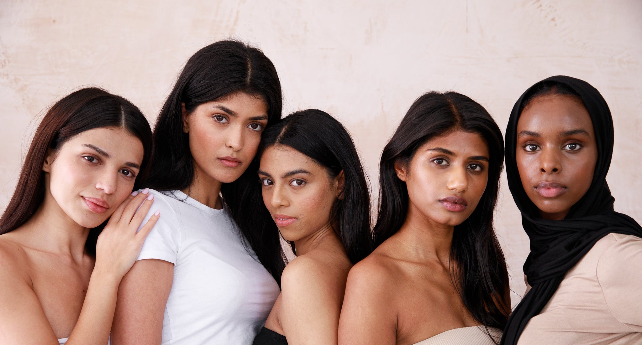 Five women with medium-to-deep golden skin tones standing together against a plain background.